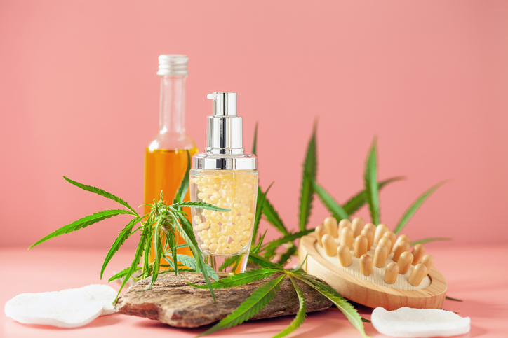 Oil lotion in bottle and leaves of hemp on a stone podium on pink background. Herbal cosmetics